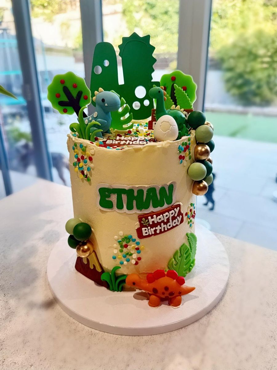 Dinosaur cake by Just In Cakes Co. Dinosaurs, trees and sprinkles, with a name on the front.
