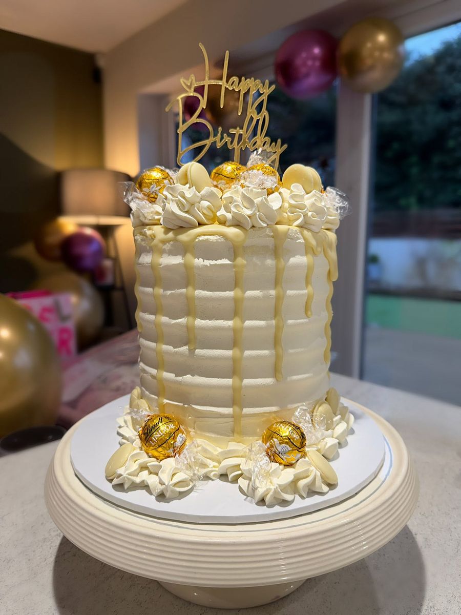 Tall buttercream birthday cake with a white chocolate drip, chocolates and a gold Happy Birthday topper