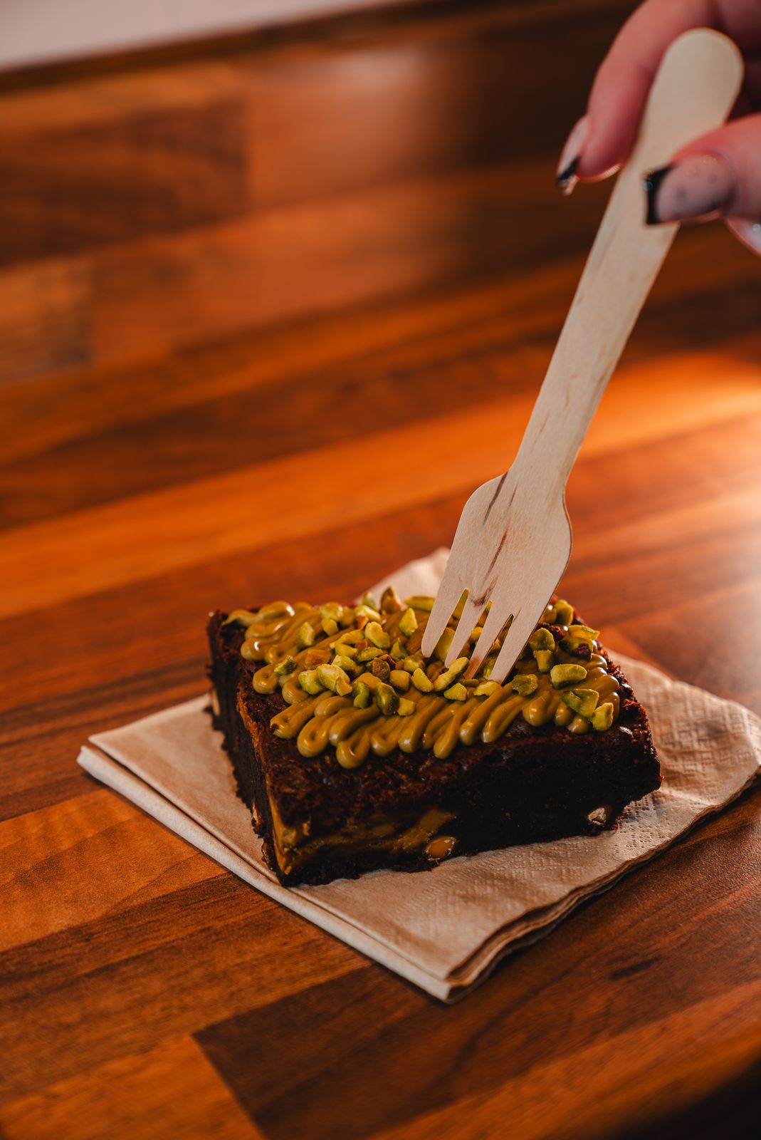 A pistachio topped brownie with a wooden fork