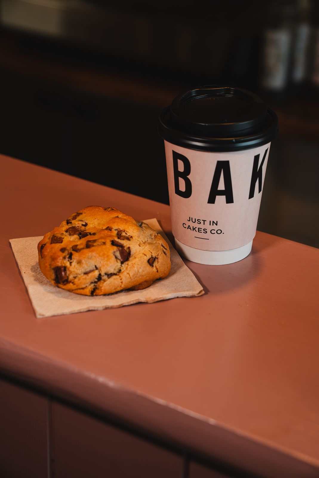 A chocolate chip cookie beside a takeaway coffee