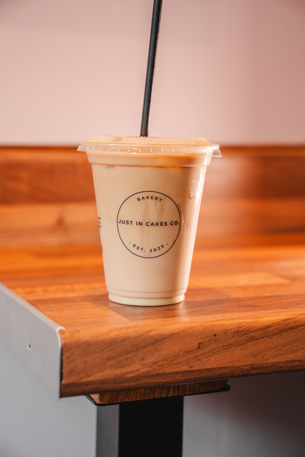 An iced latte in a Just In Cakes Co. cup on a wooden table