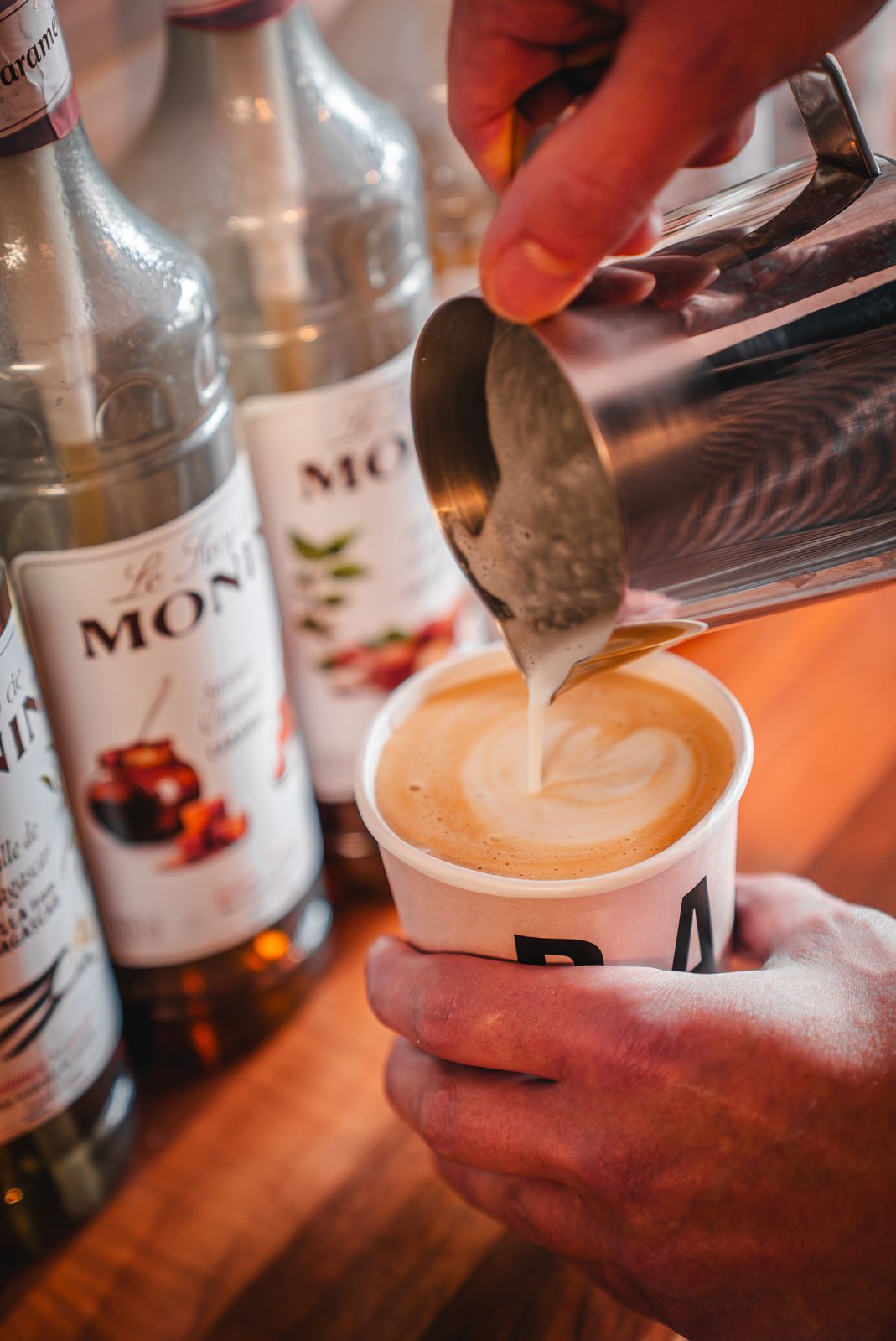 Pouring latte art into a takeaway cup in front of the syrups